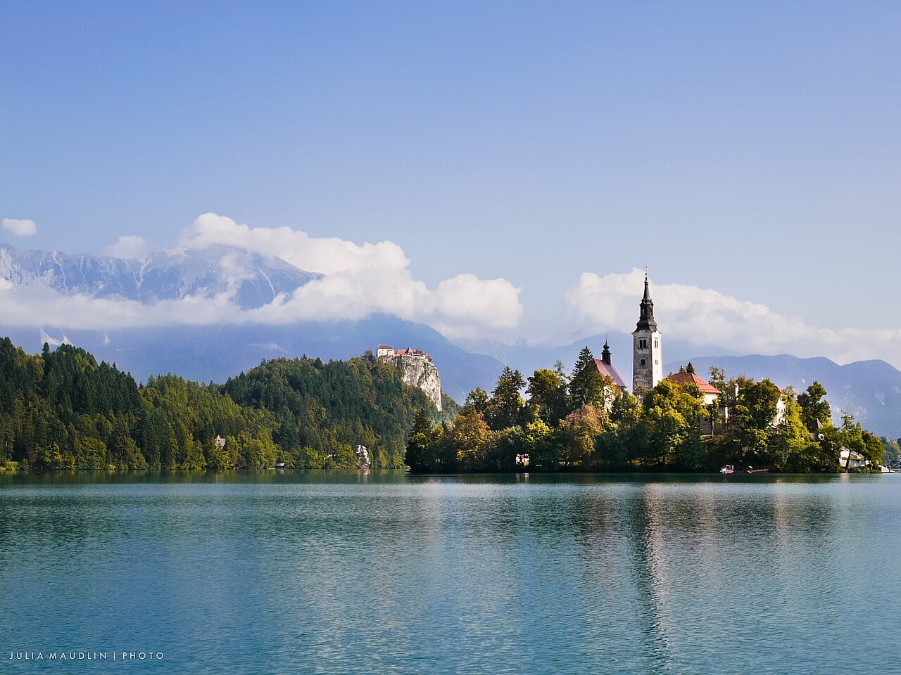 Lake Bled’s island church and castle framed by autumn trees and mountains under a blue sky