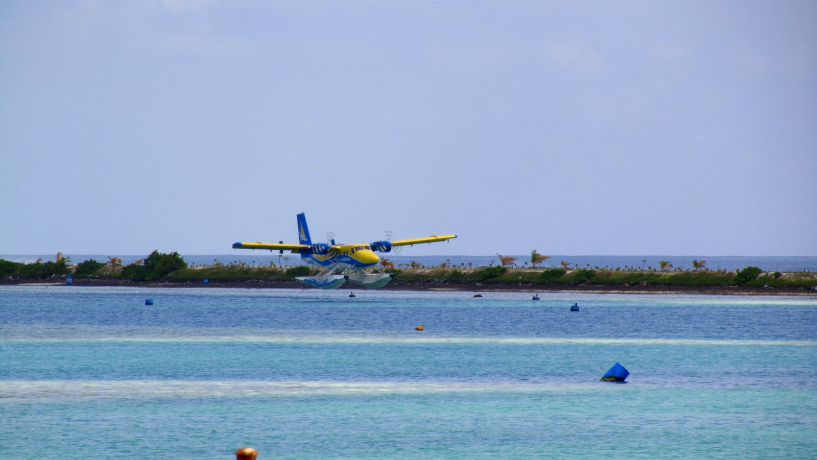 Yellow and blue Trans Maldivian Airways seaplane landing on water at Malé International Airport