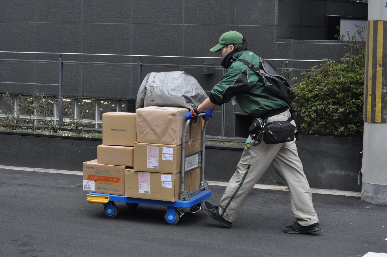 Yamato delivery worker pushing a blue trolley of parcels along a street in Osaka