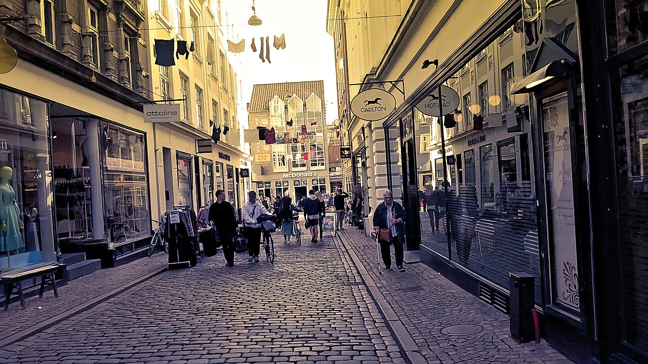 People walking and wheeling bicycles along a cobbled shopping street in Aarhus’s Latin Quarter.