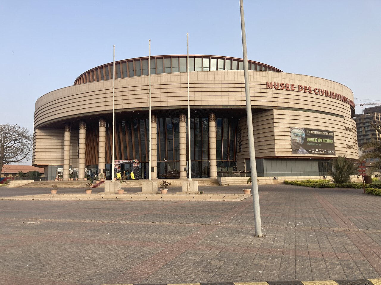 Circular façade and entrance columns of the Musée des Civilisations Noires in Dakar, seen across its paved forecourt.