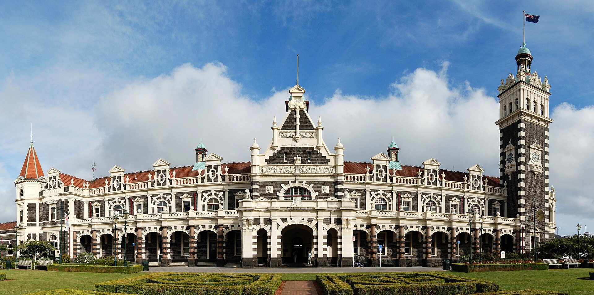 Dunedin Railway Station’s patterned dark-and-light façade, central gable and clock tower behind the formal gardens.
