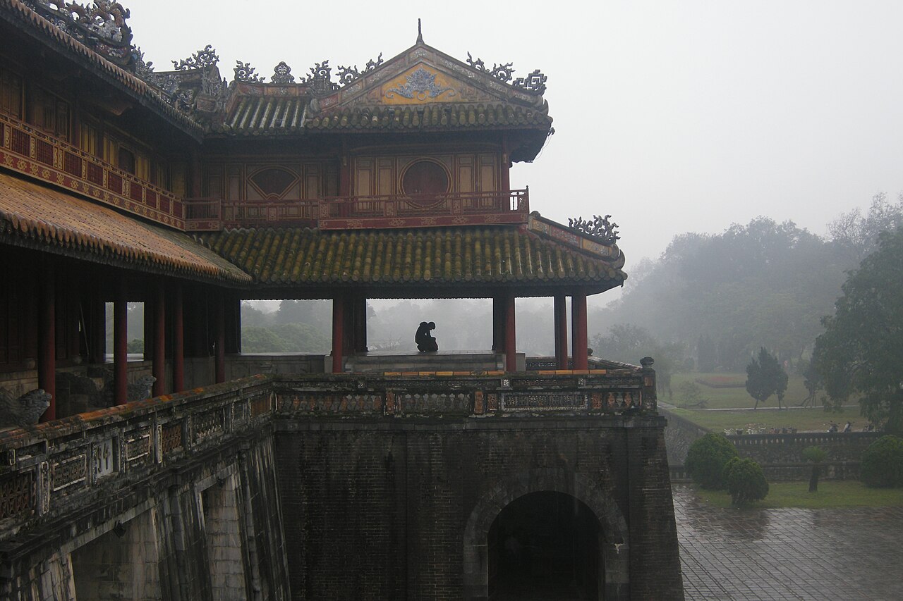 Tiled roofs and open pavilion of the Meridian Gate at Huế Imperial City, seen above the masonry gateway in mist.