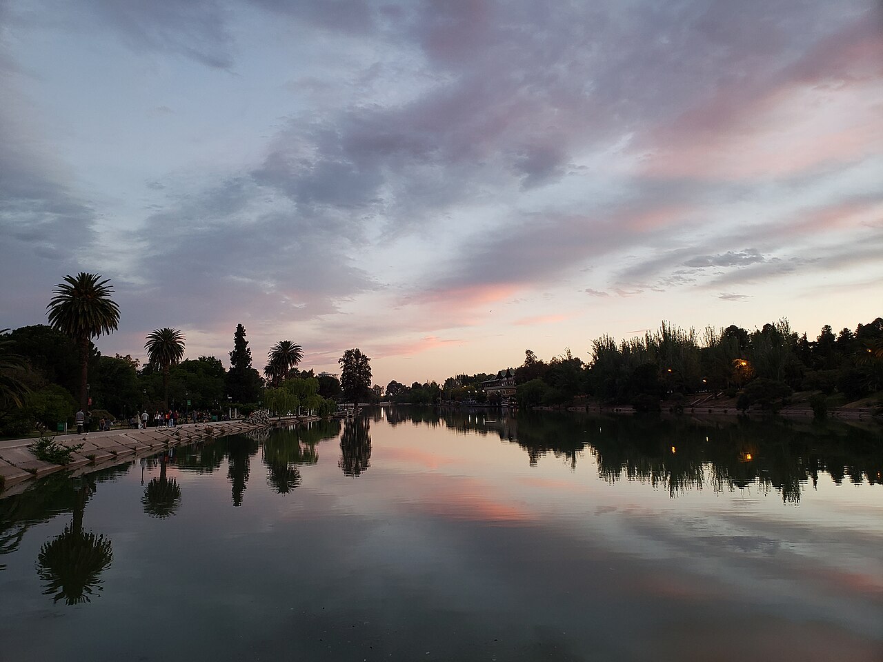 Trees and a lakeside path reflected in the lake of Parque General San Martín in Mendoza at dusk.