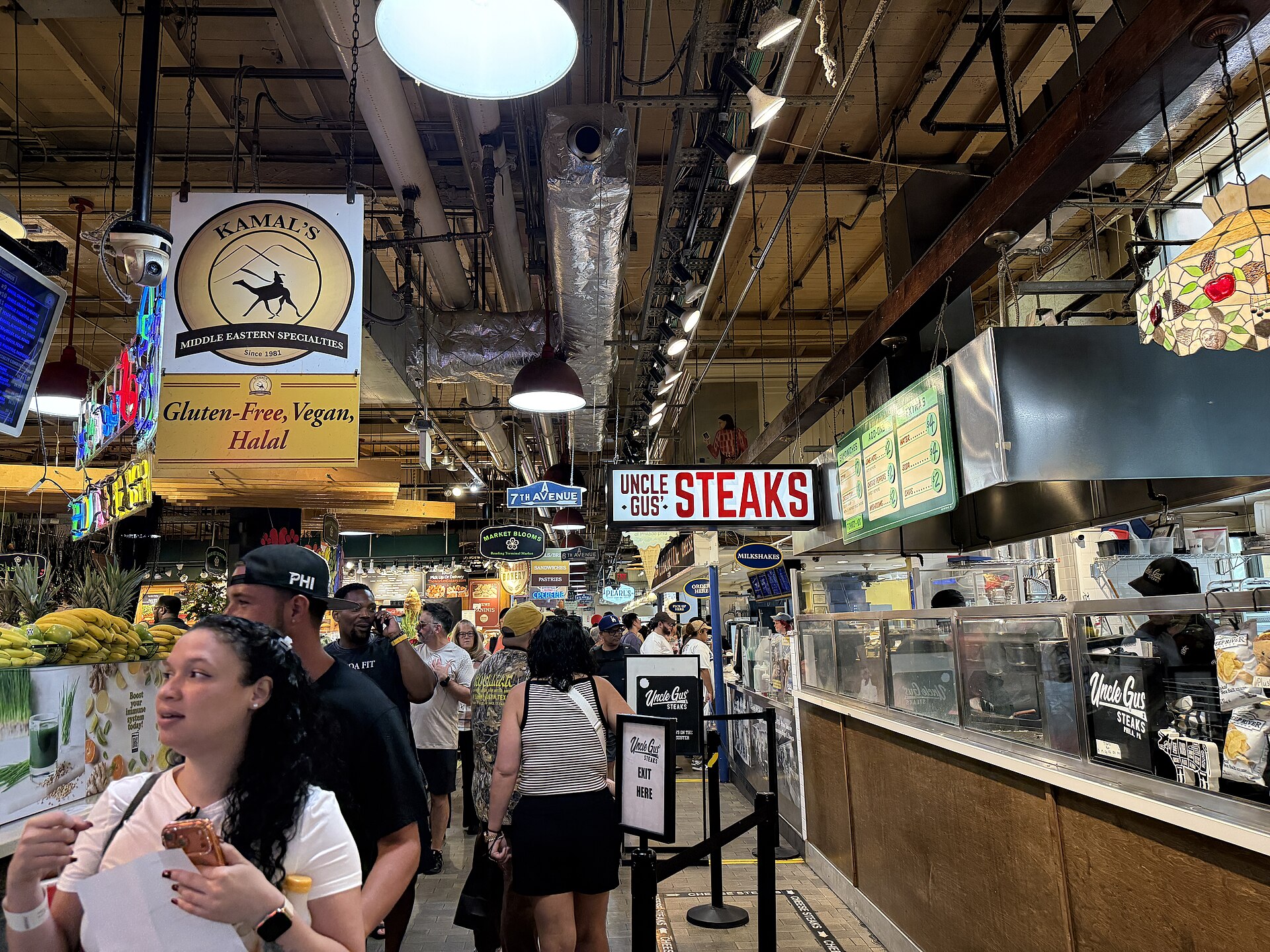 Visitors between food counters and overhead signs inside Reading Terminal Market in Philadelphia.