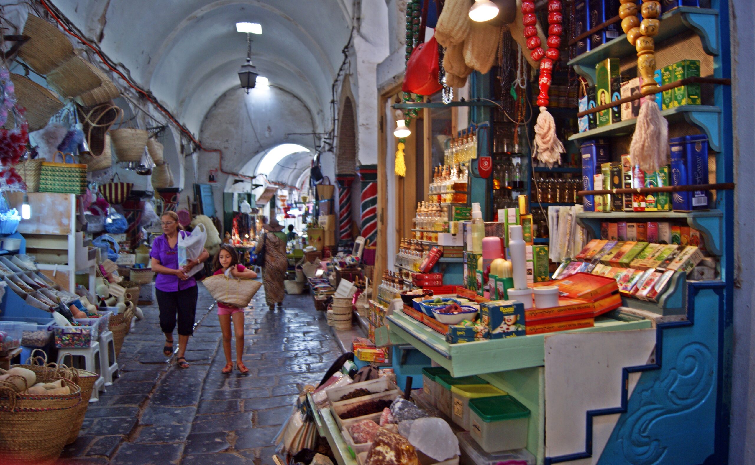 Baskets, bottles and other goods displayed along a vaulted market passage in the Tunis medina.
